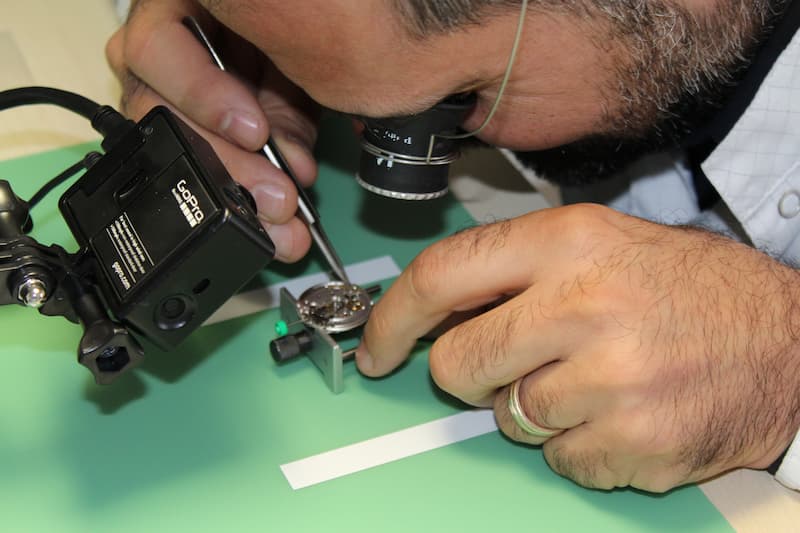 Horloger concentré assemblant un mouvement de montre, en posture stable et ergonomique.