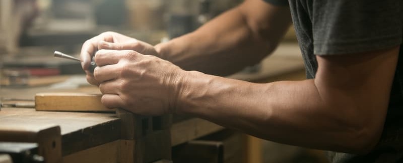 Gros plan sur les bras et les mains d’un
professionnel effectuant un travail de précision répétitif sur un établi.